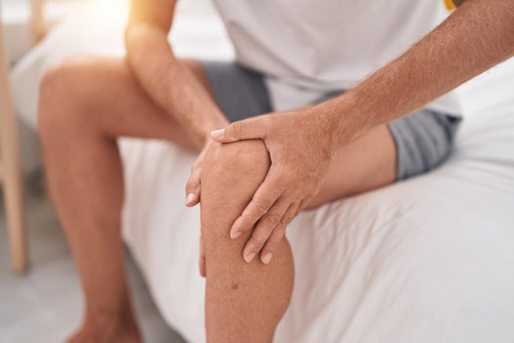 joven sentado cama dolor rodilla lesion dormitorio